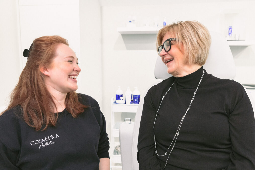 A female patient sits in the luxury treatment room of Cosmedica Aesthetics and speaks with a provider about the pelvic floor chair in Burlington.