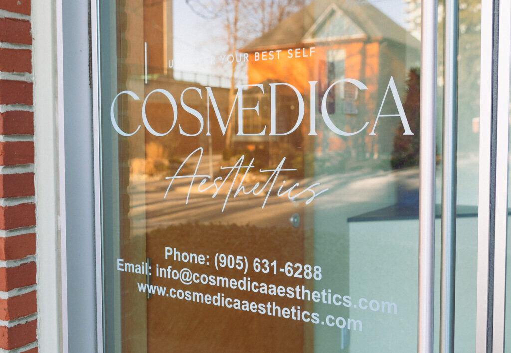 A glass front door sign for Cosmedica Aesthetics, our advanced aesthetics med spa in Burlington.