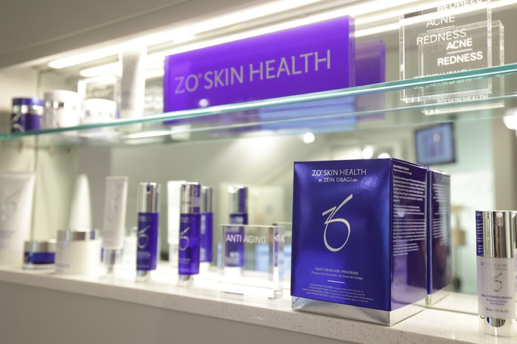 A glass shelf at Cosmedica Aesthetics holds boxes of ZO Skin Health Skincare products for patients to use after laser aesthetics in Burlington.